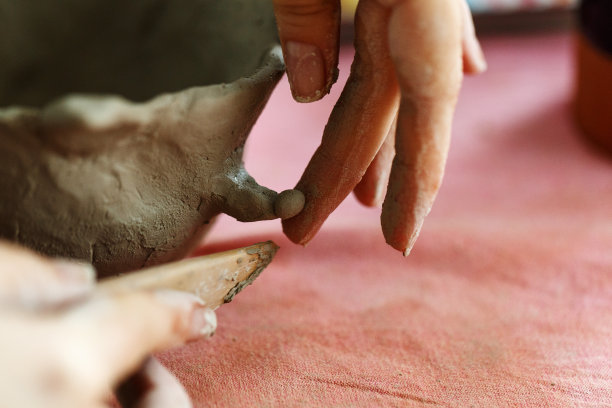 妇女们用手揉捏粘土，然后用它雕刻出杯子或碗。制作陶瓷产品的过程，特写图片下载