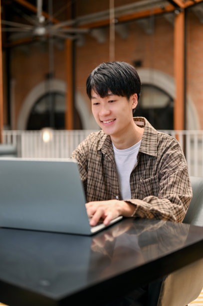 快乐的亚洲男子在户外联合办公空间远程工作，使用他的笔记本电脑。图片下载