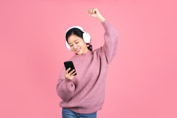 年轻可爱的亚洲女子戴着耳机听音乐和舞蹈在工作室粉红色的背景图片下载