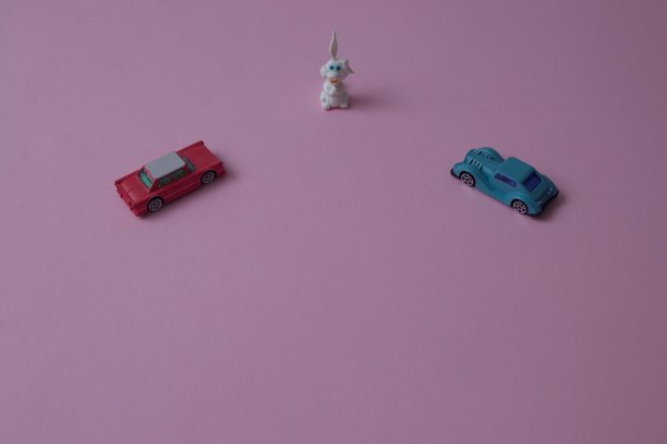 两辆车正朝着一只粉色背景上有复制空间的白兔前进。中国新年的最小构图。图片下载