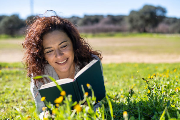 女人躺在草地上看书。图片下载