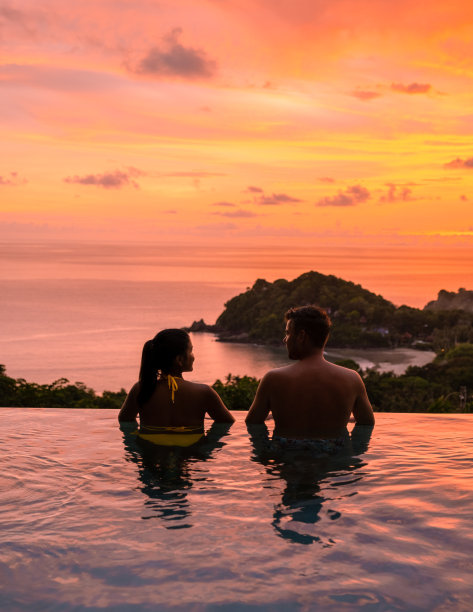 日落时分，一对年轻的男女在一个热带岛屿的游泳池边图片下载
