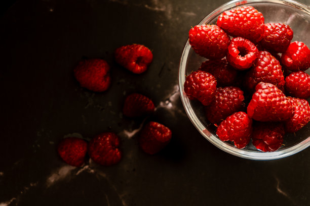 俯视图的服务在一个小碗的覆盆子在黑色花岗岩表面。黑暗食物，水平方向，文本空间。图片下载