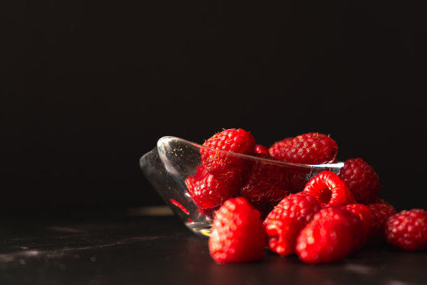 在黑色花岗岩表面上的一个小透明碗里的覆盆子的正常视图。水平方向，文本空间。图片下载