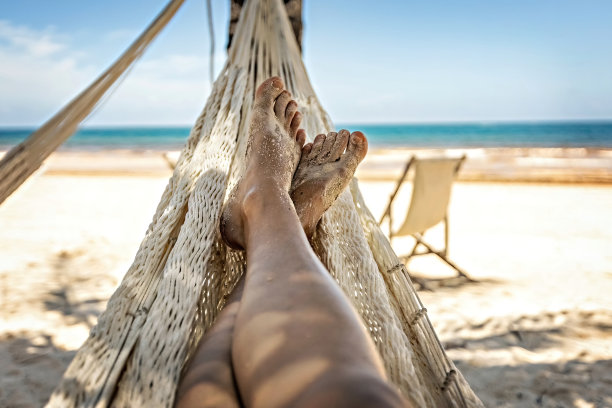 女人的腿躺在吊床上，面对着海景图片下载