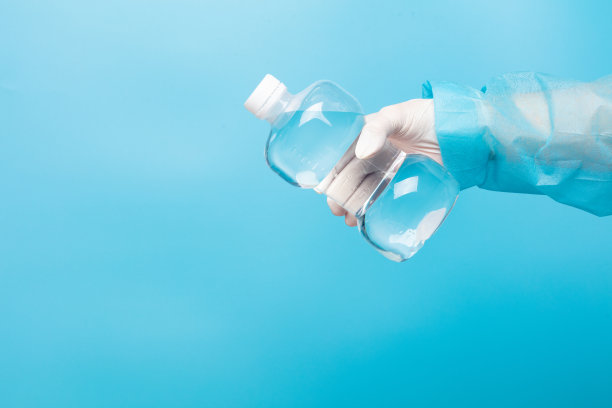 护士手拿生理盐水医用清洁液塑料瓶，戴手套，清洁干净的生理盐水塑料瓶，将无菌医用设备放在蓝色背景上隔离图片下载