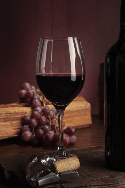 一杯红酒靠近酒瓶，放在木桌上放着葡萄图片下载