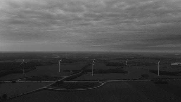 在多云的天空下，沿着道路的风力涡轮机的灰度镜头图片下载
