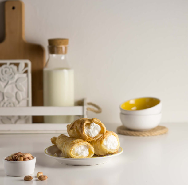 白色盘子里的奶油蛋糕。白色的桌子上有牛奶、花生。图片下载