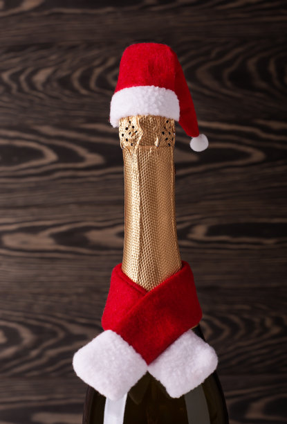 香槟瓶戴圣诞帽和红色针织围巾在木制背景。新年概念图片下载