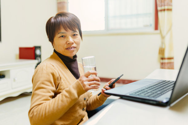 一个中年妇女正在看电脑休息，喝一杯水——简单的生活图片下载