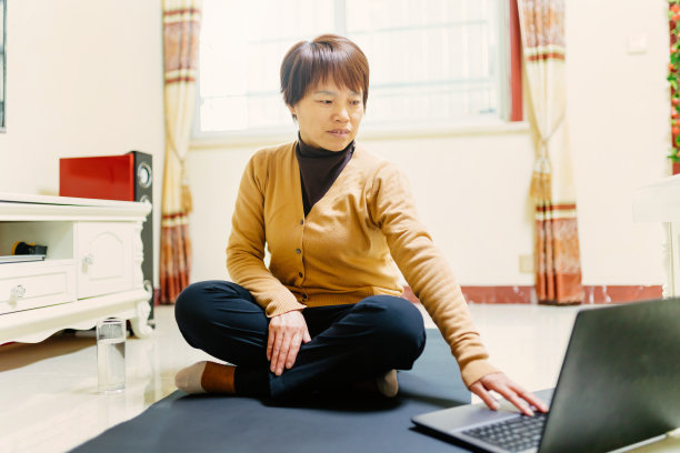 一位中年妇女在瑜伽垫上用笔记本电脑学习健身之道——科技与生活，健康的生活方式图片下载