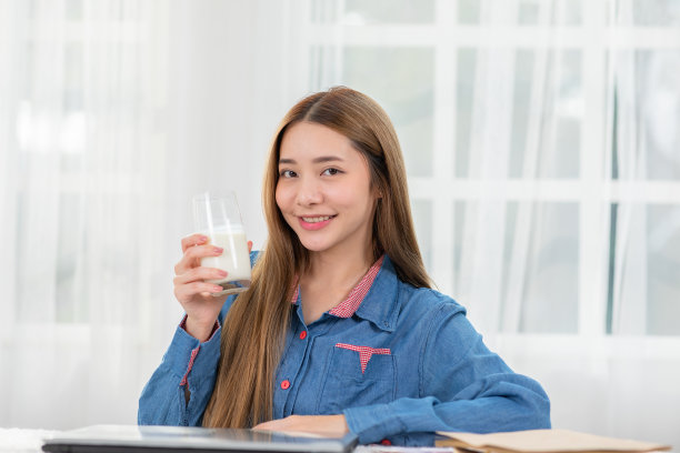 年轻的亚洲女性在家喝含钙的牛奶强健骨骼。微笑的印度妇女拿着玻璃豆浆享受营养健康的生活。天然鲜奶养生概念图片下载