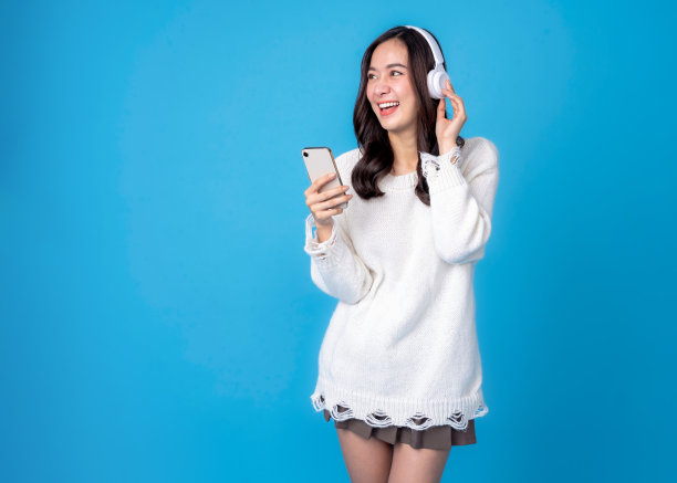 快乐的年轻女子戴着耳机听着浅蓝色背景音乐。微笑白人年轻女子听播客电子书音乐歌曲歌手摇滚乐队在耳机耳机。图片下载