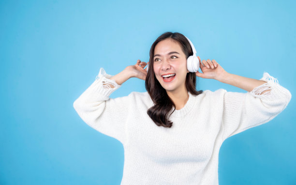 年轻的运动女人戴着耳机听音乐。音乐少女在孤立的浅蓝色背景下跳舞。美丽的女模特。图片下载