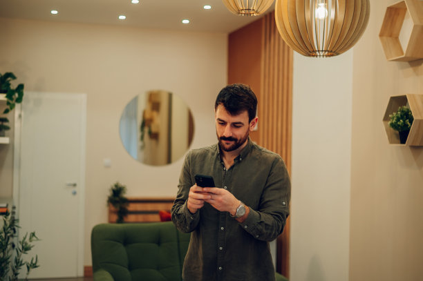 留着胡子的白人男子在家里使用智能手机图片下载