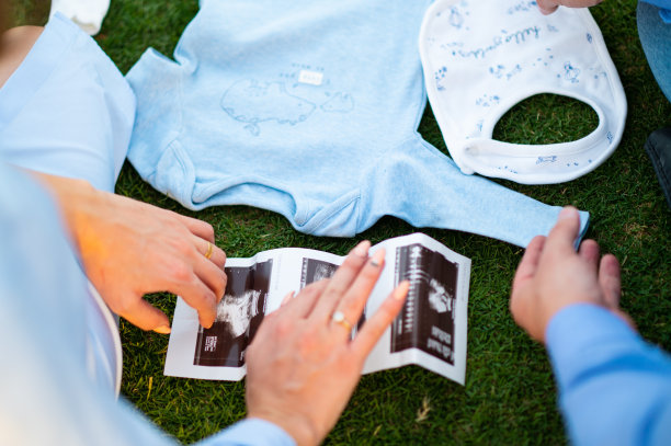 准父母为新生儿准备婴儿用品，在绿色背景下拍摄孕肚照和B超照片，孕妇正在看B超图片下载