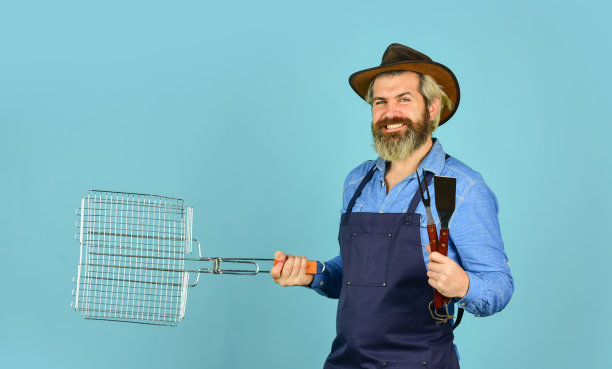 烹饪概念。单身的一天。中罕见的。工具烤肉。穿着围裙的男人拿着烧烤架。烹饪牛排。烹饪用具。农民与烧烤设备。夏季野餐。烧烤美国传统图片下载