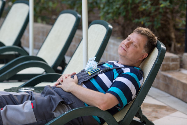 男人辛苦工作后躺在伞下的日光浴床上休息图片下载