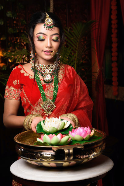 非常美丽的年轻的印度新娘的肖像在豪华的新娘服装化妆和沉重的珠宝在室内工作室照明手持莲花。婚礼时尚。图片下载