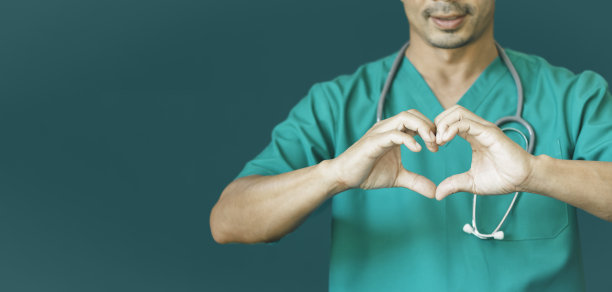 男医生的蓝绿色制服上有一个心形的手形。医疗爱、关怀和安全标志，健康保护标志概念，医务工作者用手指做一个积极的符号图片下载