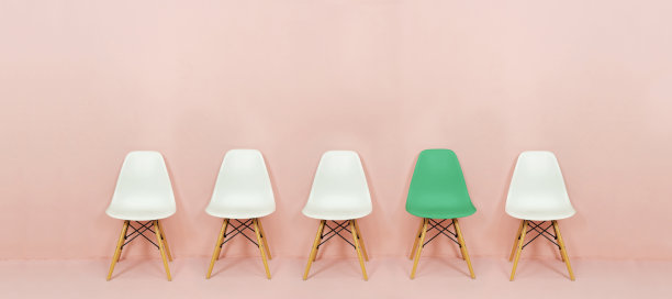 一排白色的椅子与粉红色背景上对比鲜明的绿色椅子。粉红色的墙上有五把空椅子图片下载