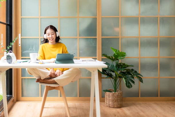 年轻女子在完成工作后，高兴地听音乐放松身心。生活方式女孩使用笔记本电脑在家里的客厅开会和工作。生活方式的概念图片下载