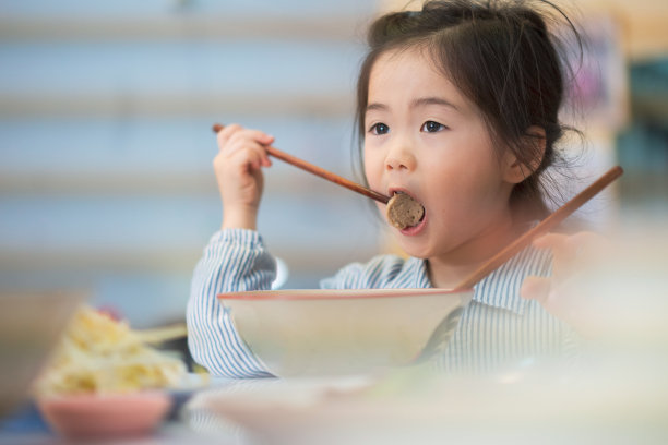 亚洲小孩用筷子吃杯子里的面条。小亚洲女孩吃早餐，脸上带着快乐的笑容图片下载