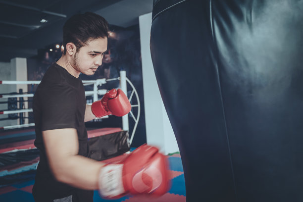 男性拳击手在拳击沙袋，年轻的男性拳击手在黑色背景上打沙袋。图片下载