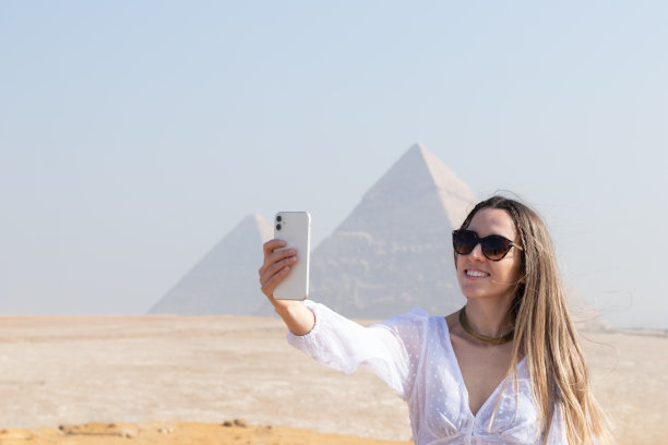 年轻漂亮的微笑女游客在模糊的背景下用金字塔自拍图片下载