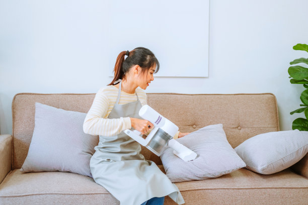 亚洲妇女用真空吸尘器清洁沙发。管理的概念图片下载