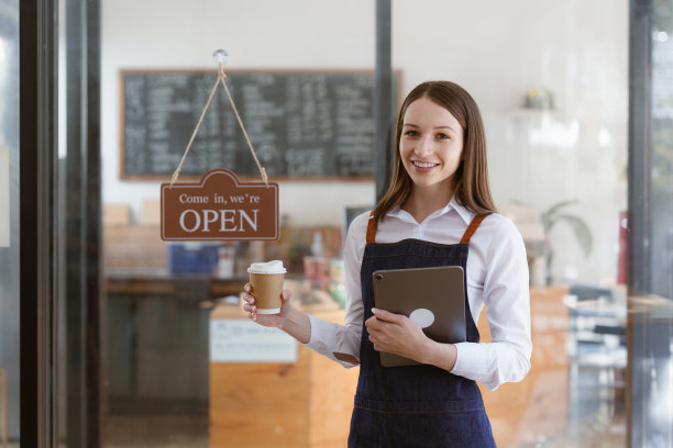年轻的女经理在餐厅与平板电脑。开着牌子的女咖啡店老板。小型企业概念图片下载