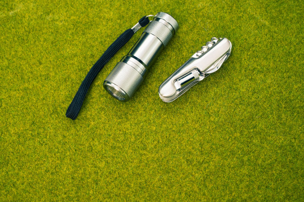 俯视图拍摄一把钢刀和一个手电筒在绿色的草地表面图片下载