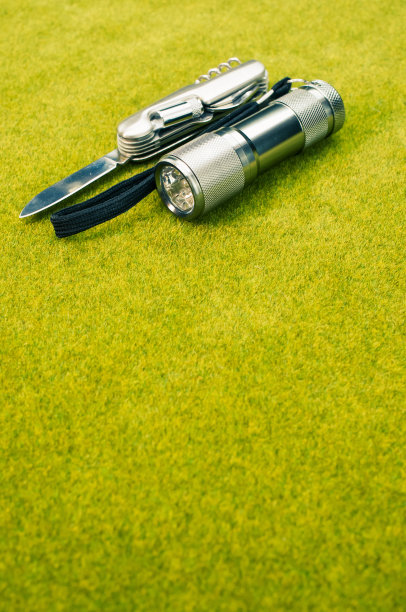 钢刀和手电筒放在绿色草地上图片下载