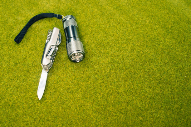 俯视图拍摄一把钢刀和一个手电筒在绿色的草地表面图片下载