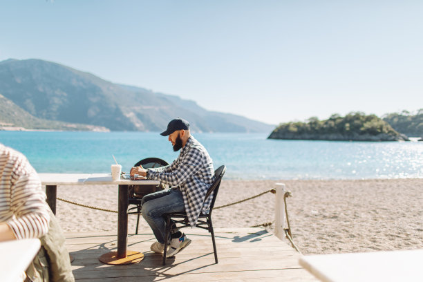 年轻的成年男子在海滩咖啡馆使用笔记本电脑工作图片下载
