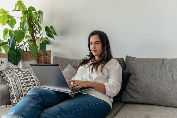 一个成年女性坐在沙发上用笔记本电脑工作图片下载