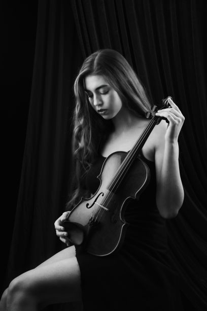 一个年轻女孩拿着小提琴坐在椅子上，背景是舞台窗帘图片下载