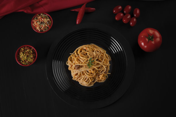 黑色盘子里盛着酱汁的意大利面，这是一张颜色较暗的摄影棚照片。图片下载