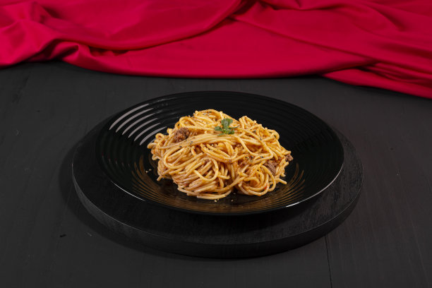黑色盘子里盛着酱汁的意大利面，这是一张颜色较暗的摄影棚照片。图片下载