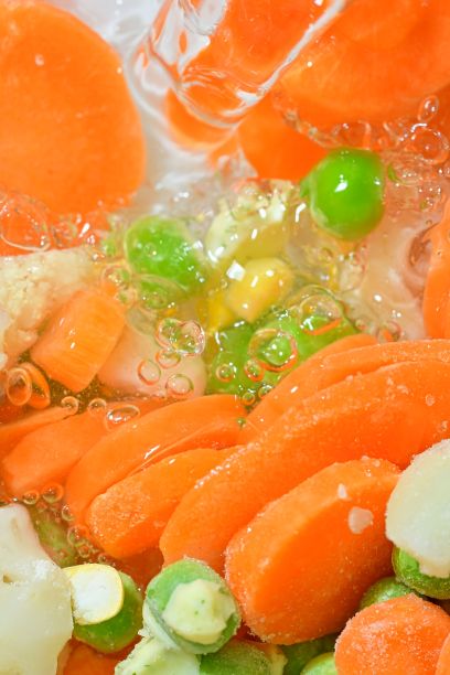 把水浇在新鲜的蔬菜汤上，白色背景上有胡萝卜、豌豆、花椰菜和玉米。白底白开水里的冷冻蔬菜汤，配上胡萝卜、豌豆、花椰菜和玉米，特写。垂直的图像。俯视图，平面设计图片下载