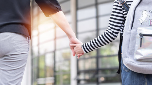 回到学校的教育理念，女孩(小学生)背着书包，拉着父母或母亲的手，走上教学楼的楼梯去上课图片下载