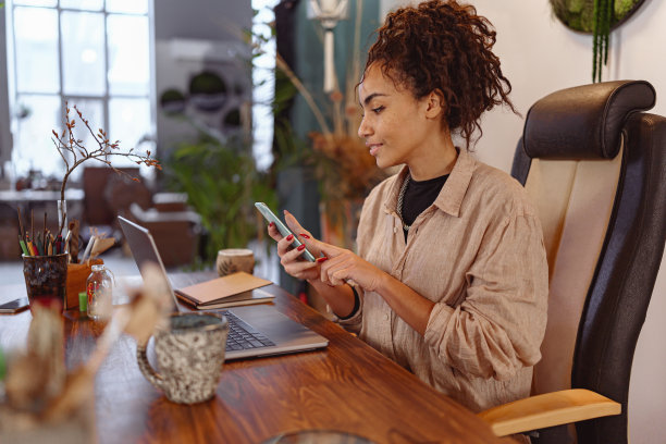 微笑的女花匠在花艺工作室的笔记本电脑上工作，用手机检查客户的订单图片下载
