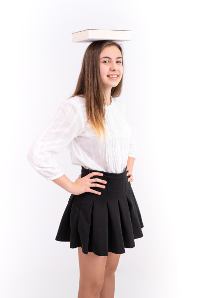 垂直拍摄的一位年轻女士头上顶着一本书，穿着黑色裙子和白色衬衫图片下载