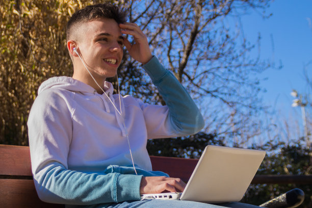 可爱的白人男孩坐在公园的长椅上，膝上放着笔记本电脑图片下载