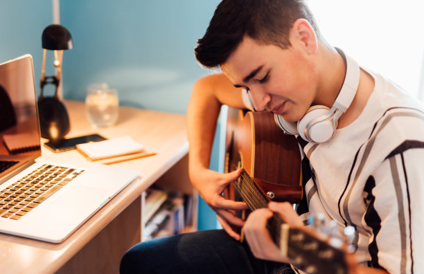 一个十几岁的男孩在你房间里在线上吉他课。技术的概念。图片下载