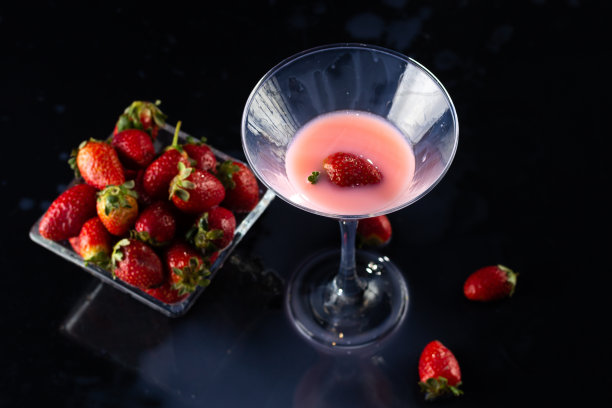 一个玻璃杯里的奶昔和一个小碗，黑色背景上有草莓图片下载