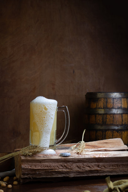 垂直镜头:木桌上的玻璃杯里盛着精酿啤酒，背景是一个木桶图片下载