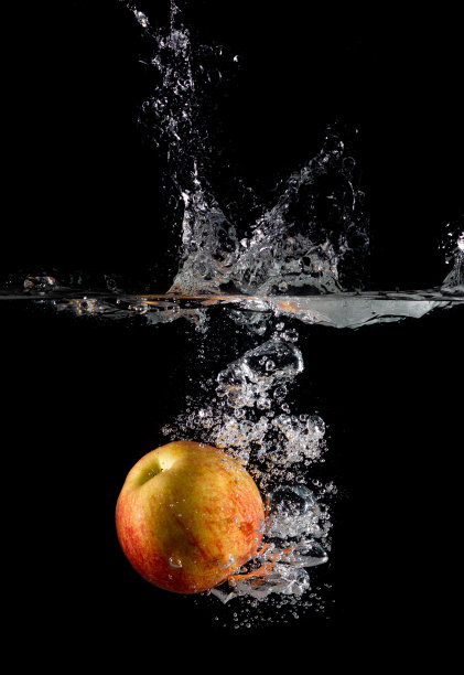 垂直拍摄水中的红苹果，在黑暗孤立的背景上溅起水花图片下载