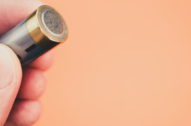 在浅橙色背景下，一只手拿着电池的特写镜头图片下载